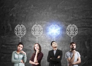 Group of people standing near chalkboard with brain sketches. One of them is shining. Concept of teamwork